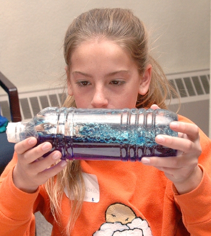 Craig Middle School seventh-grader Victoria Phelan looks at a bottle of oil, water, and food coloring meant to simulate tsunami waves at a Science Explorers workshop.