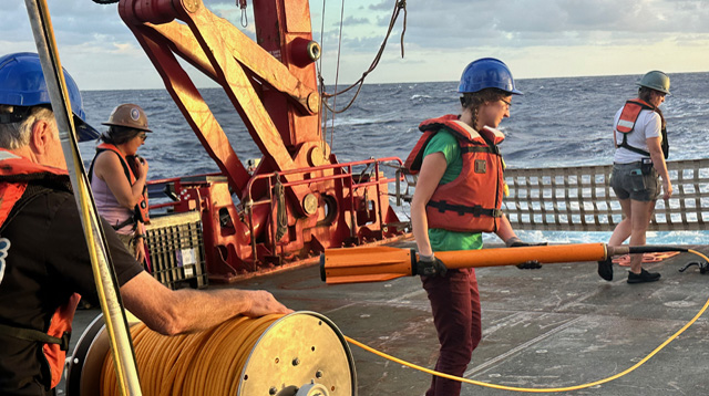 Hannah Mark holding a magnetometer onboard a scientific ship