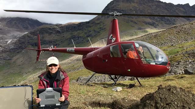 Meghan Miller with seismic station installation and red helicopter in Alaska